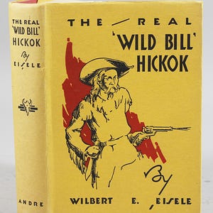 Könnte beinhalten: Ein Vintage-Buch mit dem Titel "The Real 'Wild Bill' Hickok" von Eisele. Das Cover ist gelb mit einer roten Illustration eines Mannes mit Hut und Pistole. Der Buchrücken ist ebenfalls gelb mit Titel und Autorennamen.