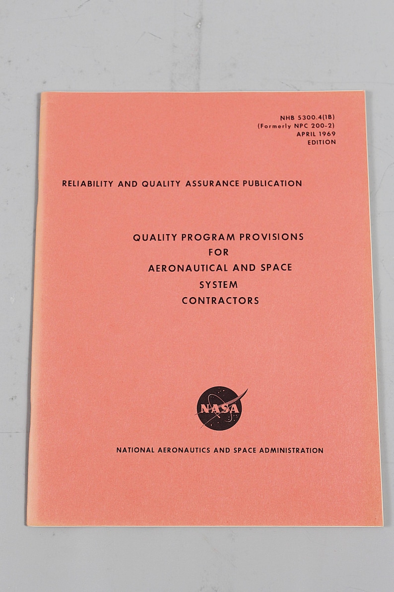 Pu&ograve; includere: Una pubblicazione NASA vintage color corallo intitolata "Reliability and Quality Assurance Publication". Il documento include il logo NASA e il testo che descrive le disposizioni del programma di qualit&agrave; per gli appaltatori aeronautici e spaziali. L'edizione &egrave; dell'aprile 1969.