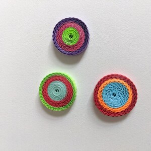 May include: Three colourful paper quilled circles with concentric rings of different colours. The circles are arranged in a triangular pattern on a white background.