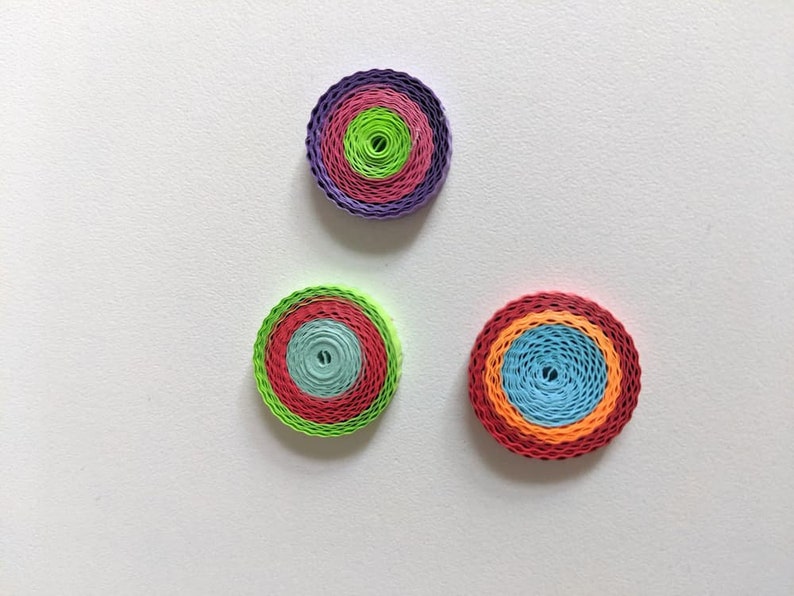 May include: Three colourful paper quilled circles with concentric rings of different colours. The circles are arranged in a triangular pattern on a white background.