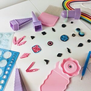 May include: A set of tools for paper quilling, including a variety of tools for shaping and curling paper, a comb for smoothing paper, and a variety of templates for creating different shapes. The tools are arranged on a white surface with a variety of paper quilling projects.