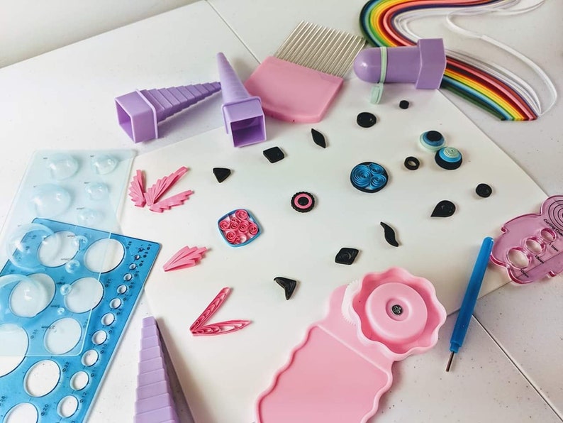 May include: A set of tools for paper quilling, including a variety of tools for shaping and curling paper, a comb for smoothing paper, and a variety of templates for creating different shapes. The tools are arranged on a white surface with a variety of paper quilling projects.