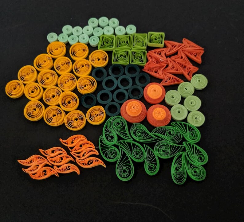 May include: A colourful assortment of paper quilling designs in green, orange, and yellow. The designs include circles, squares, swirls, and leaves.