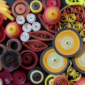 May include: A close-up of a colourful paper craft art piece. The art is made of many different coloured paper rolls, creating a variety of shapes and patterns. The colours include yellow, orange, red, brown, black, and white.