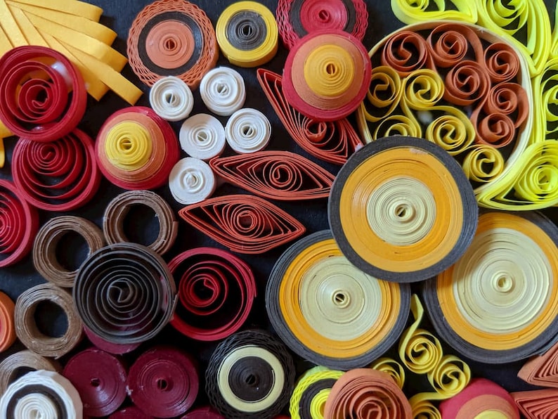 May include: A close-up of a colourful paper craft art piece. The art is made of many different coloured paper rolls, creating a variety of shapes and patterns. The colours include yellow, orange, red, brown, black, and white.