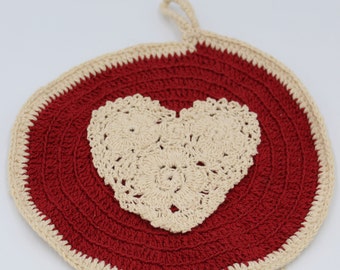 May include: A red and cream crocheted pot holder with a heart-shaped design in the center.