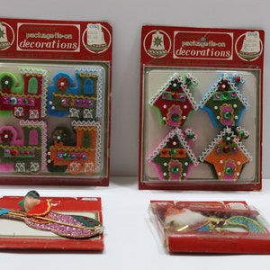 May include: Four packages of vintage Christmas decorations. Two packages contain felt houses with glitter and beads. One package contains a felt train with glitter and beads. One package contains a felt angel with glitter and beads. The packages are all red and white with the text "package tie-on decorations".