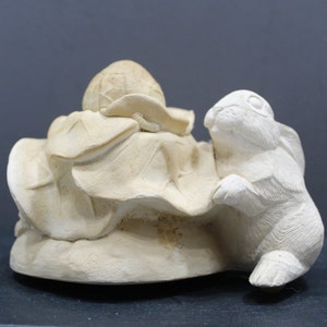 May include: A white ceramic sculpture of a rabbit looking at a turtle with its shell covered in leaves. The sculpture is a whimsical and charming piece of art.