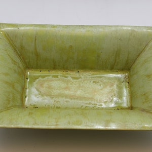May include: A rectangular ceramic dish with a light green glaze. The dish has a slightly raised rim and a smooth, glossy finish.