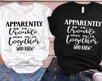 May include: Two white t-shirts with black text that reads "Apparently we're trouble when we're together. Who knew?"