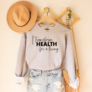 Könnte beinhalten: Ein graues Sweatshirt mit dem Text "Transform Health for a living" in Schwarz gedruckt.