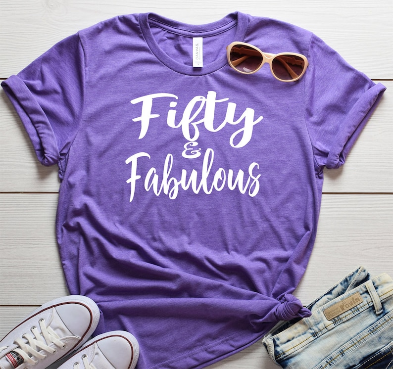 May include: Purple t-shirt with white text that reads "Fifty & Fabulous".