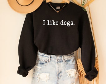 May include: Black sweatshirt with the text "I like dogs." in white lettering. The sweatshirt is worn over a pair of light blue denim shorts.