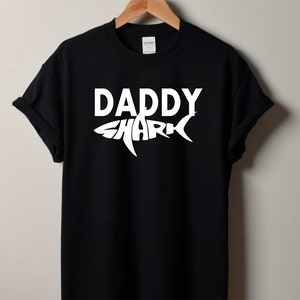 May include: Black t-shirt with a white graphic of a shark with the word "Daddy" inside the shark's body.