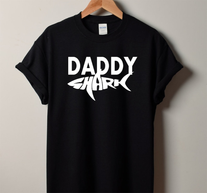 May include: Black t-shirt with a white graphic of a shark with the word "Daddy" inside the shark's body.