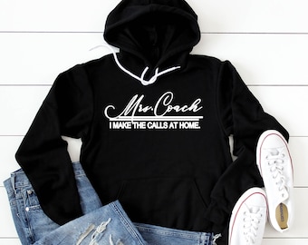 Peut inclure: Sweat-shirt à capuche noir avec un texte blanc qui dit "Mrs. Coach I make the calls at home."