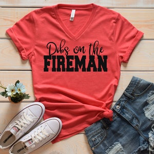 May include: Red V-neck t-shirt with the text "Dibs on the FIREMAN" in black lettering.
