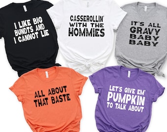 May include: Five different t-shirts with Thanksgiving-themed text printed on them. The shirts are in various colors, including black, white, gray, orange, and purple. The text on the shirts includes "I like big bundts and I cannot lie", "Casserolin' with the hommies", "It's all gravy baby baby", "All about that baste", and "Let's give em' pumpkin to talk about".