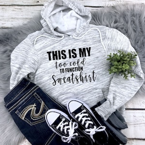 May include: Gray and white hooded sweatshirt with the text "This is my too cold to function sweatshirt" in black.