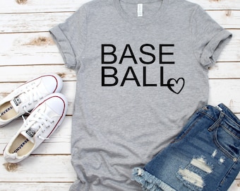 May include: Gray t-shirt with the text "BASE BALL" and a heart symbol. The shirt is paired with denim shorts and white sneakers.