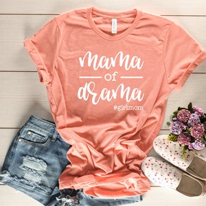 May include: A coral pink t-shirt with the text "mama of drama #girlmom" in white.