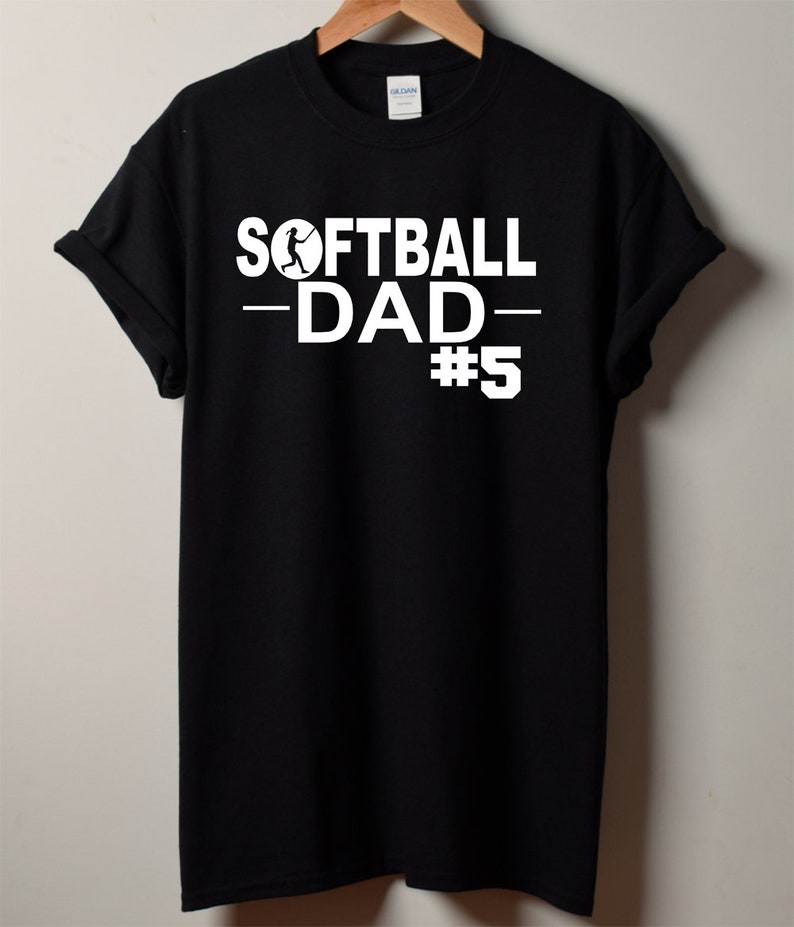 May include: Black t-shirt with white text that reads "Softball Dad #5" with a softball player graphic.