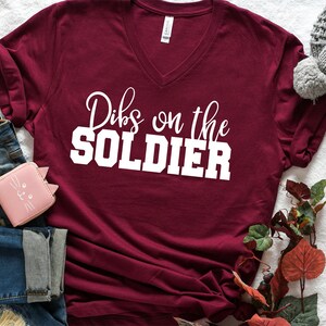 Op de afbeelding: Een bordeauxrood t-shirt met V-hals en de tekst "Dibs on the SOLDIER" in wit.
