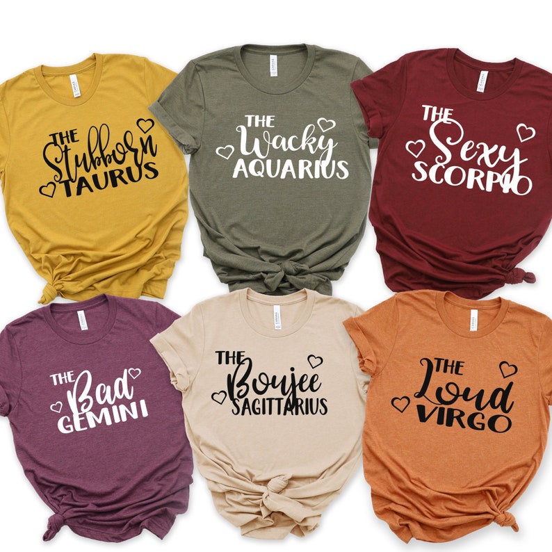 Puede incluir: Seis camisetas coloridas con texto tem&aacute;tico del zodiaco. Las camisetas son de color amarillo mostaza, verde oliva, burdeos, beige y naranja. Cada camiseta presenta un signo zodiacal diferente con un adjetivo l&uacute;dico, como "Stubborn Taurus" y "Wacky Aquarius".