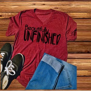 May include: Red V-neck t-shirt with the text "Beautifully Unfinished" in black lettering.