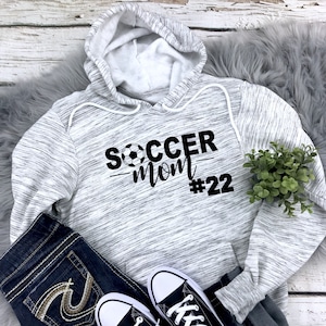 May include: Gray and white heather hoodie with black text that reads "Soccer Mom #22" with a soccer ball graphic.