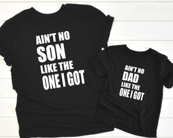 May include: Two black t-shirts with white text. The larger shirt says "Ain't no son like the one I got". The smaller shirt says "Ain't no dad like the one I got".