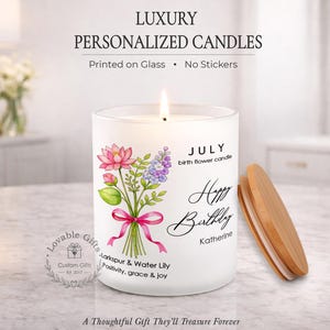 May include: A white personalized candle with a floral design and the text "Happy Birthday Katherine." The candle has a wooden lid and the text "July birth flower candle." The candle reads "Lovable Gifts Custom Gifts Est. 2017."