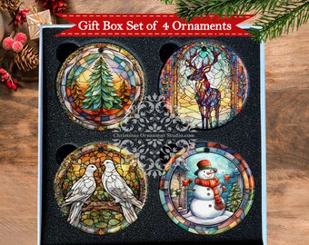 May include: A set of four round Christmas ornaments in a gift box. The ornaments feature stained glass designs of a Christmas tree, a deer, a pair of doves, and a snowman. The ornaments are in a blue and white gift box with black foam inserts.