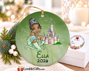Op de afbeelding: Een rond groen keramieken ornament met een tekenfilmfiguur met een tiara in een groene jurk, een kasteel en de tekst Ella 2026. Het ornament heeft een gouden ophangkoord en een subtiel damastpatroon op het oppervlak.