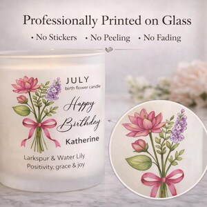 May include: A white glass candle with a floral design and the text "Happy Birthday Katherine." The design includes pink lotus flowers, purple larkspur, and a pink ribbon. The candle is labeled "July birth flower candle."