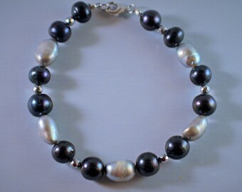 May include: A black and white pearl bracelet with a silver clasp. The bracelet is made of alternating black and white pearls.