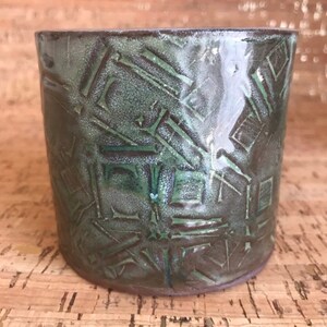 May include: A green ceramic planter with a geometric pattern. The planter has a slightly textured surface and a rounded shape.