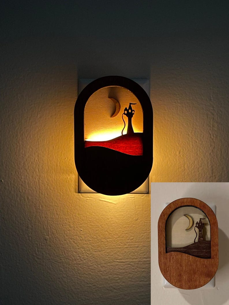 May include: A wooden night light with a silhouette of a cat in a tower with a crescent moon in the background. The night light is lit and casts a warm glow on the wall.