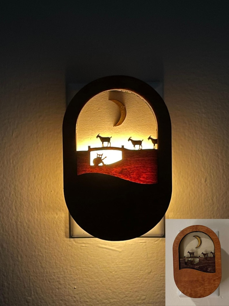 May include: A wooden night light with a crescent moon and goats silhouetted against a red and brown background. The night light is lit and glows warmly.