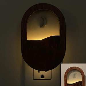 May include: A wooden nightlight shaped like a crescent moon with a wave design. The nightlight is plugged into an electrical outlet and is lit up.