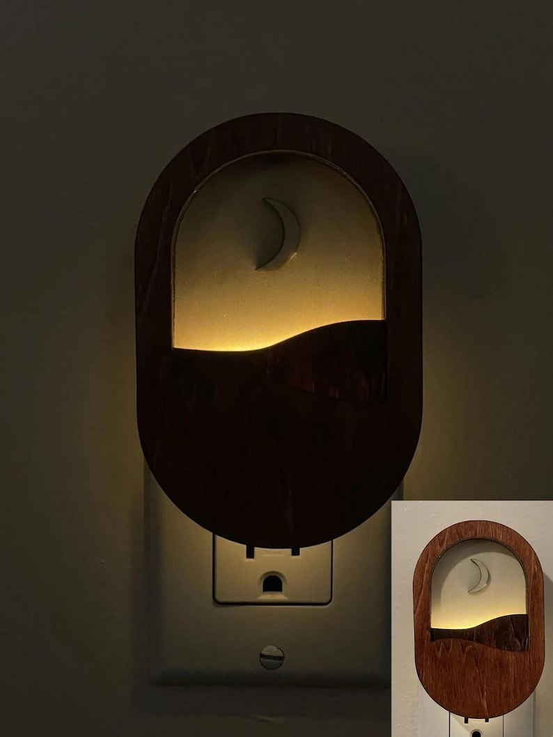 May include: A wooden nightlight shaped like a crescent moon with a wave design. The nightlight is plugged into an electrical outlet and is lit up.