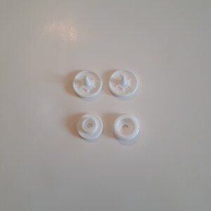 May include: Four white plastic snap fasteners, two with a raised center and two with a recessed center.