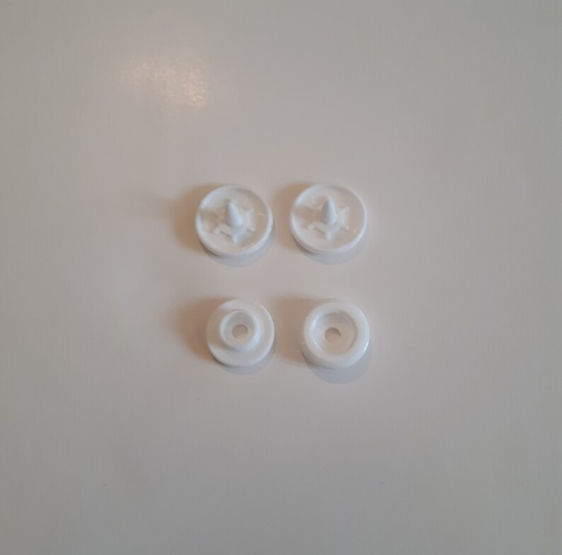 May include: Four white plastic snap fasteners, two with a raised center and two with a recessed center.