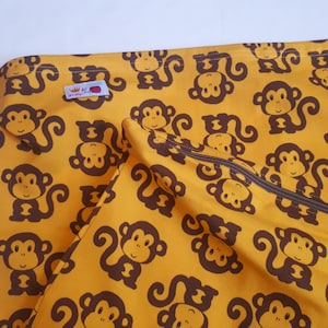 Puede incluir: Una bolsa amarilla de cordón con un patrón de mono marrón. La bolsa tiene un cierre de cremallera y una pequeña etiqueta roja con el texto "King of the Jungle".