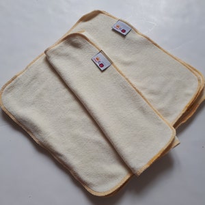 May include: Two beige cloth burp cloths with yellow trim and a small red and yellow logo that says "Little Crown" on each cloth.