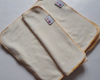 Puede incluir: Dos paños de eructos de tela beige con ribete amarillo y un pequeño logotipo rojo y amarillo que dice "Little Crown" en cada paño.