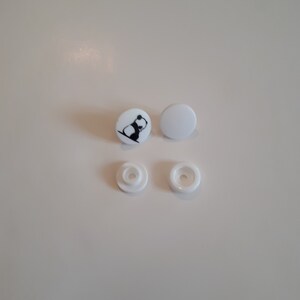 May include: Four white plastic snap buttons, two with a black and white panda design.