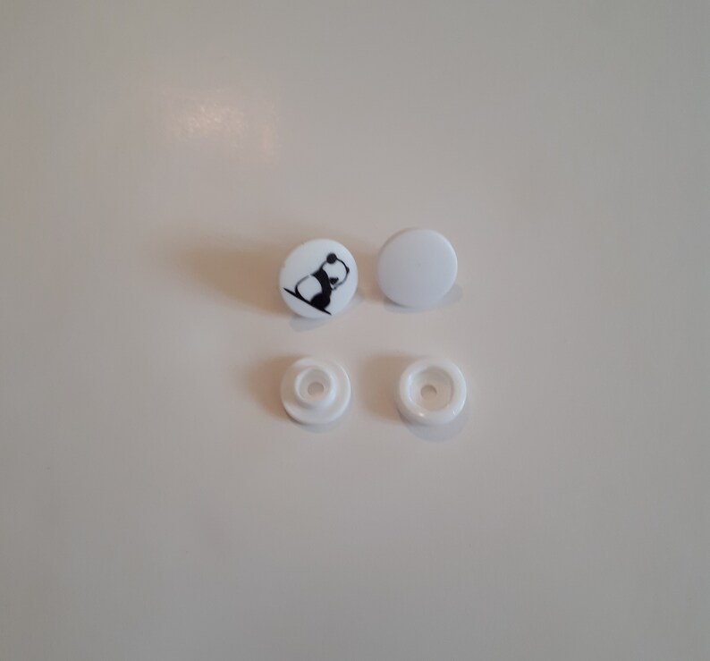 May include: Four white plastic snap buttons, two with a black and white panda design.