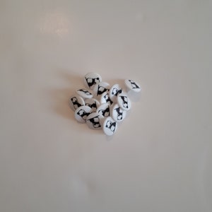May include: A pile of white plastic buttons with a black panda bear design.