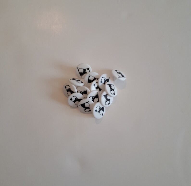 May include: A pile of white plastic buttons with a black panda bear design.